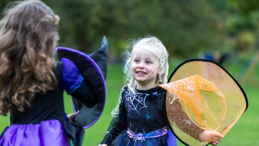 Two girls play wearing black and purple witches costumes and an orange pointed witch hat.